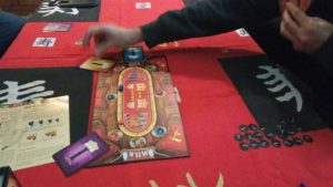 Imagen del juego, el tablero en el centro y dos cartas ya jugadas sobre este con valor 1, un jugador está colocando una carta de valor 1 también en una casilla vacía.